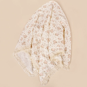 Detail of floral baby muslin blanket featuring pink flowers and cream tassel fringe