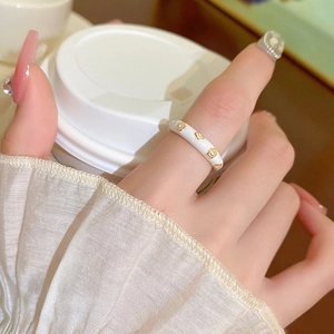 Detail of white enamel ring with gold floral patterns on finger with elegant cuff