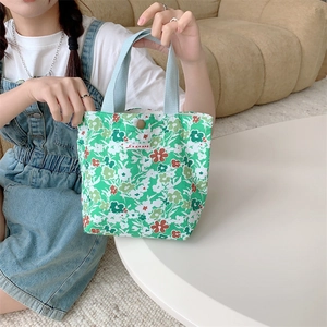 Dettaglio ravvicinato di una borsa in tela floreale con manici azzurri ed etichetta logo