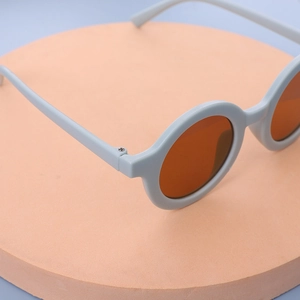 Detailed view of kids round candy color sunglasses with amber lenses on a stand
