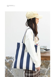 Detail of blue and white striped canvas tote bag with woven brand label on model side view