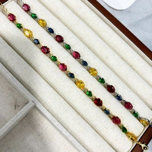 Close-up of gold and silver bracelets with colorful oval gemstones in a beige jewelry box