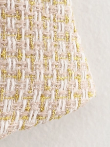 Detailed macro view of tweed fabric in cream and pink tones with sparkling gold threads