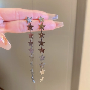 Detail of silver-toned star tassel earrings with brushed metal finish held by hand