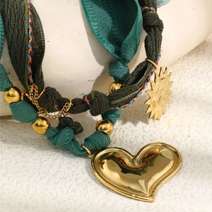 Detailed macro of gold heart and sun charms on a green textured fabric necklace strap