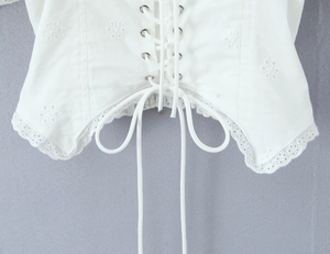 Primer plano de blusa blanca de algodón con bordado floral, encaje y detalles de cordones
