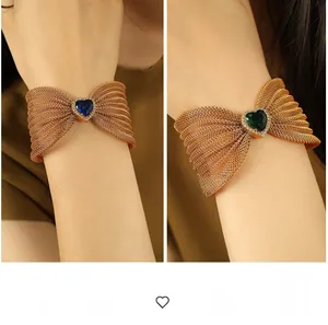 Detail of woven mesh bow bracelet featuring heart-shaped blue and emerald gemstones