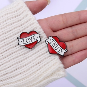 Set of heart enamel pins with LOVE and TRUE ribbons pinned on a white knit sweater