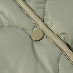 Macro shot of diamond quilting patterns and a matte snap button on a green jacket