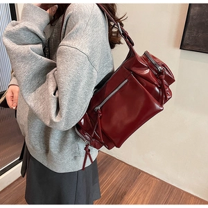 Détail du sac à bandoulière en cuir bordeaux avec de multiples poches zippées et lanières