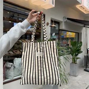 Vertical black and white striped canvas tote bag held by hand in an outdoor setting
