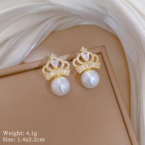 Detail shot of golden crown earrings with white pearls and zircons on silk background