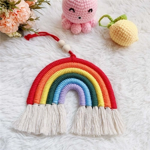 Handwoven rainbow cotton wall hanging with wooden beads and tassels on a plush white rug