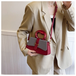 Detail of a color-block handbag with red metal handle and golden H-shaped clasp