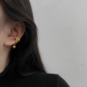 Golden ear cuff with layered rhinestone bands and a dangling heart pendant on a model