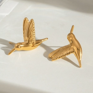 Minimalist gold hummingbird stud earrings in stainless steel on white stone surface