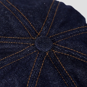Détail d'une casquette en denim bleu montrant le bouton supérieur et les coutures