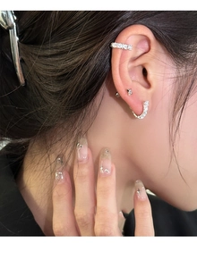 Close-up of stacked silver U-shaped earrings and star studs with zircon on ear