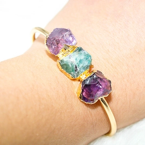 Detail of gold-plated cuff featuring raw amethyst and emerald green crystals on wrist