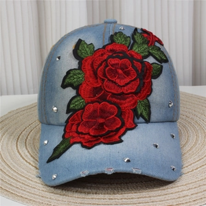 Close-up of denim baseball cap featuring red rose embroidery and silver metal rivets