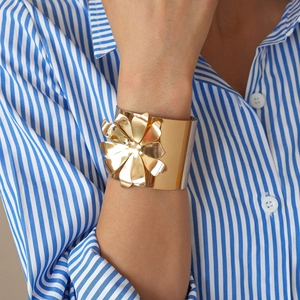 Detail shot of a wide gold metal cuff with a 3D floral design on a model's wrist