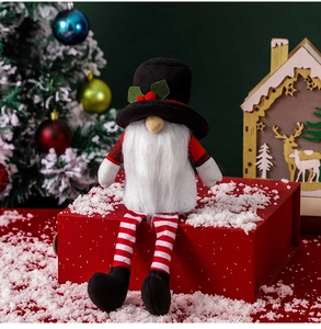 Close-up of a festive plush Christmas gnome sitting on a red gift box in a snowy scene