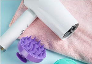 Detail view of purple silicone scalp massager brush and white hair dryer on pink towel