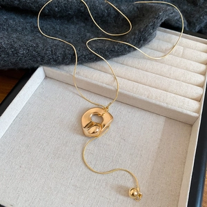 Goldene Halskette mit unregelmäßigem Anhänger und Quasten auf einer Schmuckschatulle