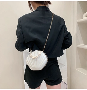 Rear view of a model wearing a white shell-shaped acrylic bag with gold metal chain strap