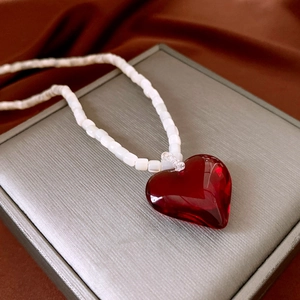 Detail of red heart pendant on white beaded necklace displayed on luxury velvet