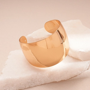 Detailed view of wide gold cuff bracelet on white marble with polished mirror finish