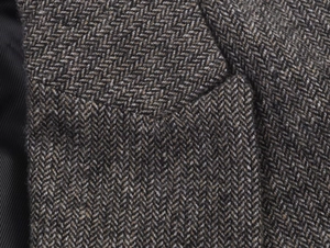 Macro shot of grey and brown herringbone tweed fabric with detailed stitching and texture