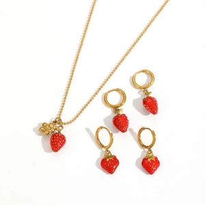 Close-up of strawberry pendant jewelry set with golden beaded necklace and hoop earrings