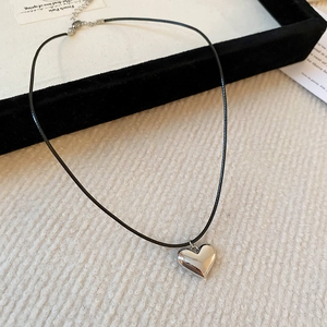 Macro detail of silver heart pendant on black cord necklace with lobster clasp closure