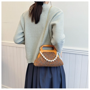 Brown tweed evening bag with a vintage wooden handle and pearl chain detail worn by model