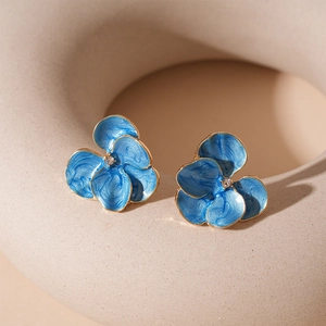 Detail of blue flower stud earrings with gold trim and crystal center on beige background