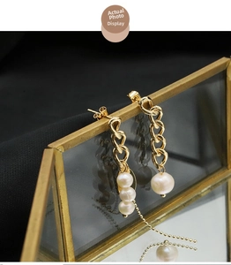 Detail of baroque pearl tassel earrings with asymmetrical gold chains on glass frame