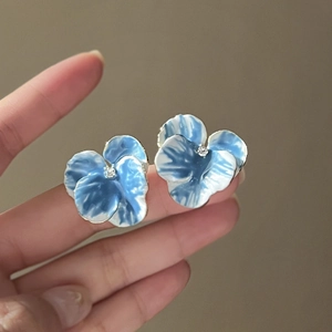 Macro detail of iris blue and white floral stud earrings with gradient enamel finish