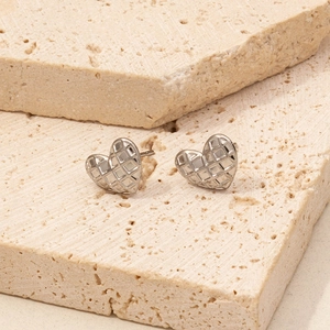 Macro shot of silver heart stud earrings with quilted pattern on beige stone pedestal