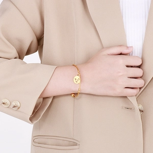 Detailed view of gold stainless steel smiley face charm bracelet on a female model wrist