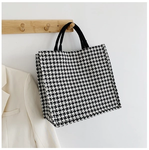 Classic black and white houndstooth tote bag hanging on wooden hook with beige blazer