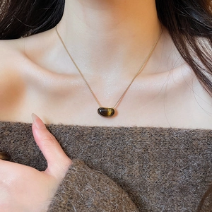 Close-up of a vintage tiger eye stone pendant necklace worn over a brown sweater