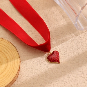 Dettaglio choker in velluto rosso con ciondolo a cuore glitterato e bordo dorato