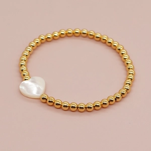 Detail of beaded bracelet featuring gold metal beads and white heart-shaped shell charm