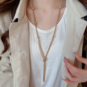 Detail of a gold multilayer knotted tassel necklace worn by a model over a white shirt