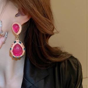 Detailed view of layered teardrop earrings with pink resin and magenta stones on a model