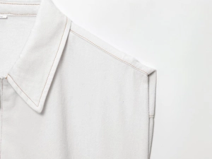Détail d'un gilet en jean blanc montrant des surpiqûres orange et le tissu en sergé