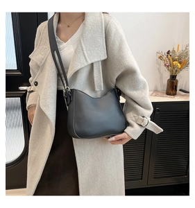 Close-up of black crescent crossbody bag with adjustable strap worn on beige coat