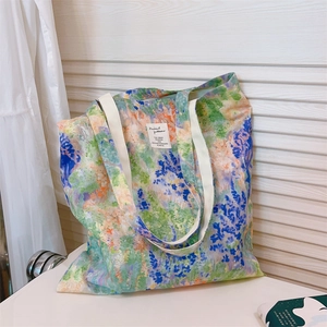 Detail of floral canvas tote bag showing wide white strap and artistic label on wooden wall
