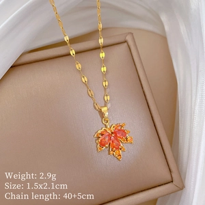 Close-up of golden maple leaf pendant with orange gemstone on beige jewelry box